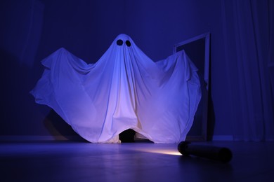 Creepy ghost. Woman covered with sheet in blue light, low angle view
