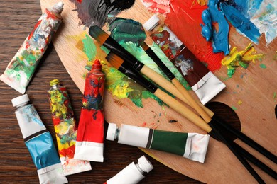 Photo of Tubes with oil paints, brushes and palette on wooden table, flat lay