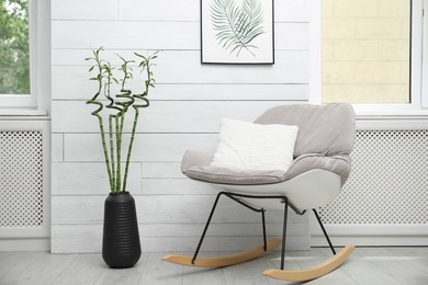 Photo of Vase with green bamboo stems and stylish rocking chair in room. Interior design