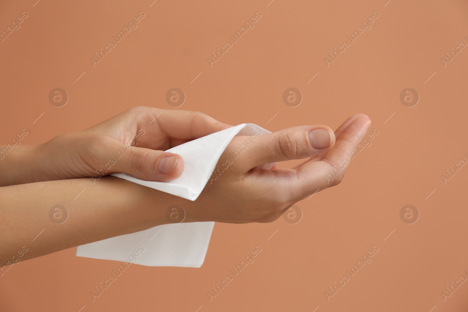 Photo of Woman cleaning hands with paper tissue on light brown background, closeup