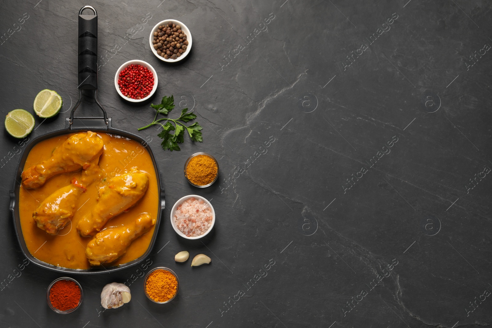 Photo of Tasty chicken curry and ingredients on black textured table, flat lay. Space for text