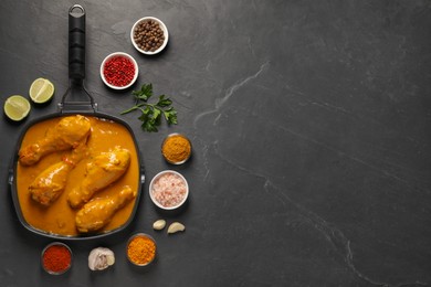 Photo of Tasty chicken curry and ingredients on black textured table, flat lay. Space for text