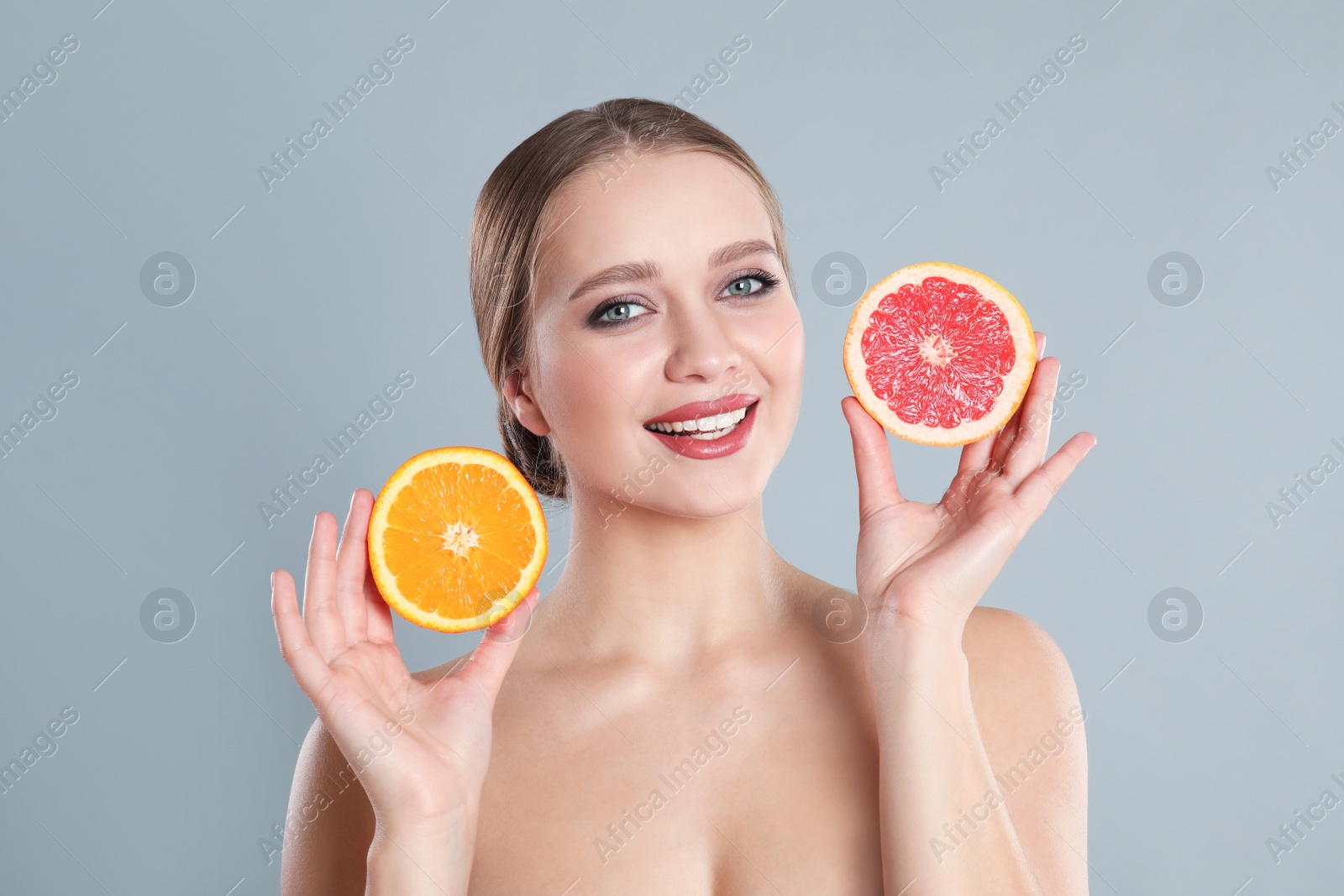 Photo of Young woman with cut orange and grapefruit on grey background. Vitamin rich food