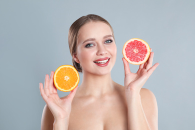 Young woman with cut orange and grapefruit on grey background. Vitamin rich food