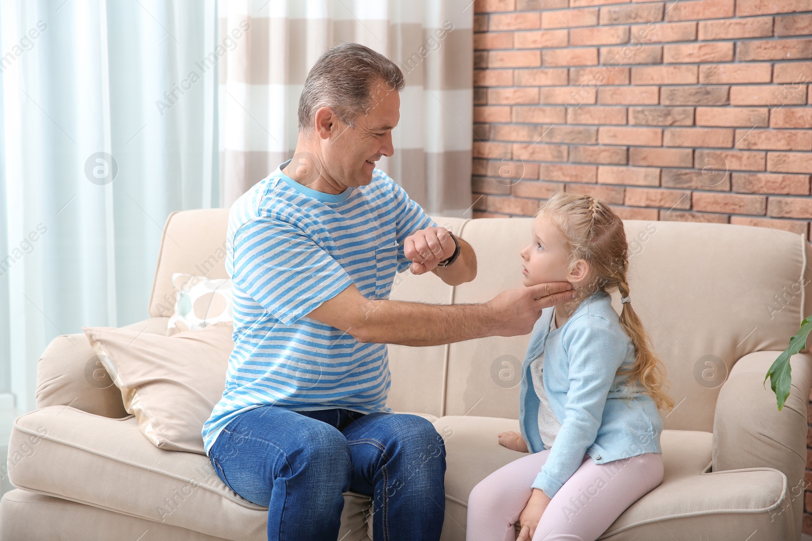 Photo of Mature man checking little girl's pulse with fingers at home