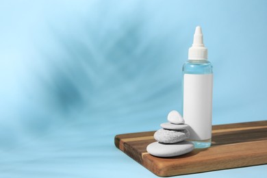 Photo of Cosmetic product, stacked stones and shadow of tropical leaf on light blue background. Space for text