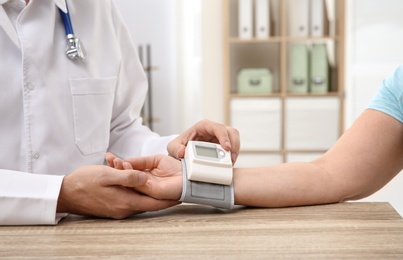 Doctor checking mature woman's pulse with medical device in hospital, closeup