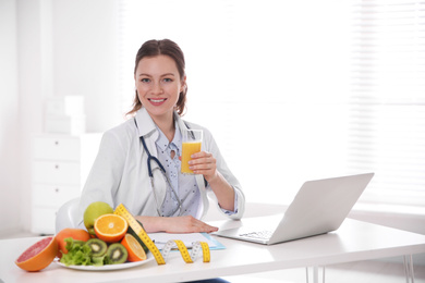 Nutritionist with glass of juice and laptop at desk in office