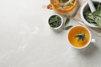 Photo of Sage tea and green leaves on light grey marble table, flat lay. Space for text