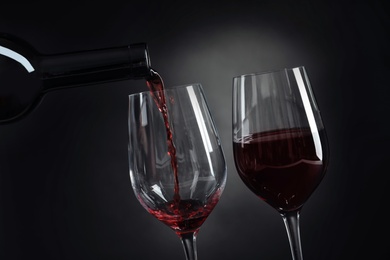 Photo of Pouring delicious red wine into glass on dark background