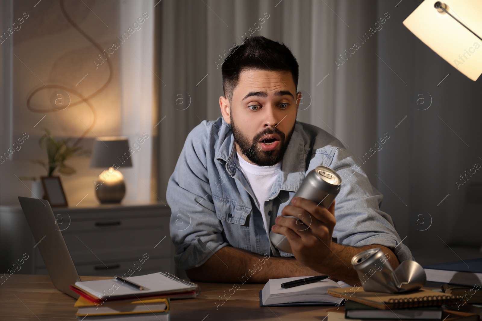 Photo of Emotional young man with energy drink studying at home