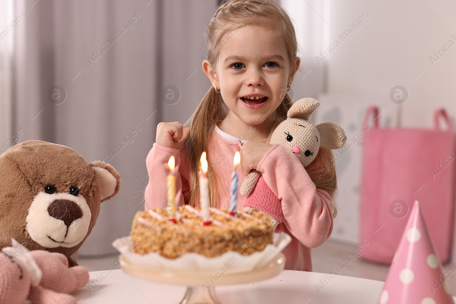 Photo of Cute girl with birthday cake and toys at table indoors