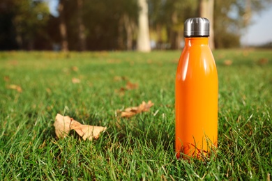 Photo of Modern orange thermos bottle on green grass outdoors. Space for text