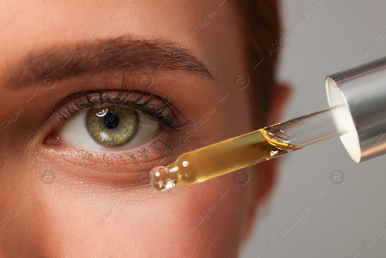 Photo of Beautiful young woman applying cosmetic serum onto her face on grey background, closeup