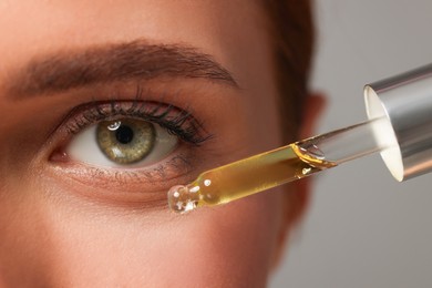 Photo of Beautiful young woman applying cosmetic serum onto her face on grey background, closeup