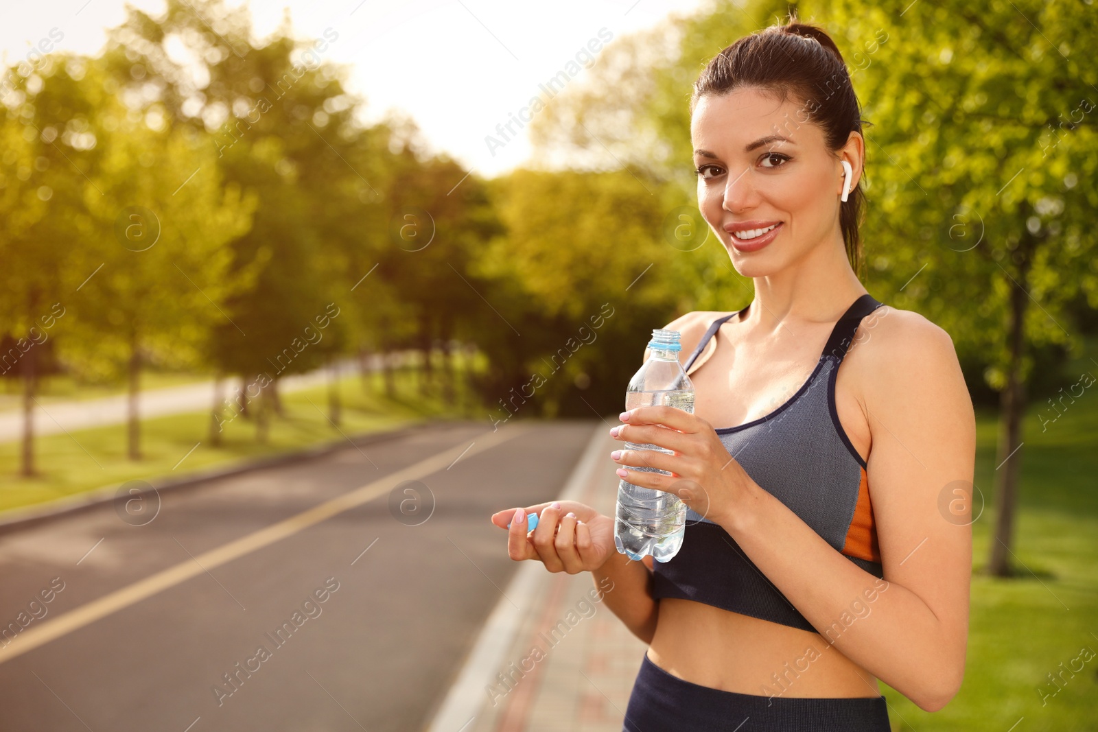Photo of Beautiful woman in fitness clothes with bottle of water outdoors