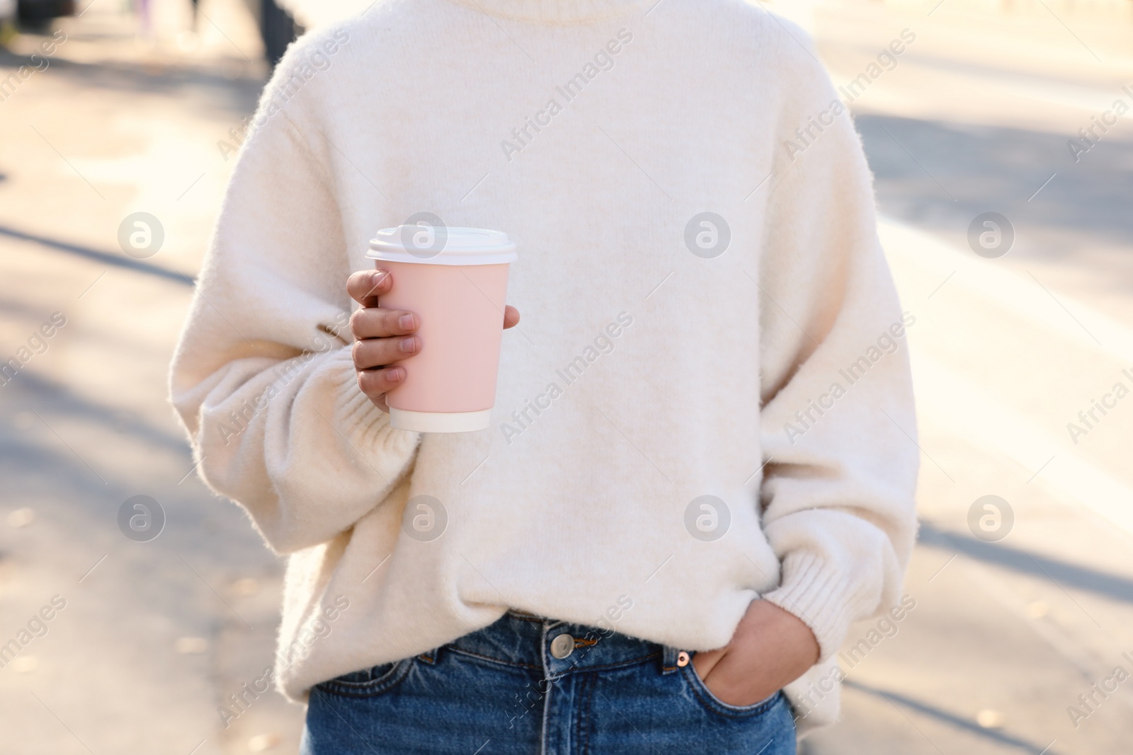 Photo of Woman holding pink takeaway cardboard cup on city street, closeup. Coffee to go