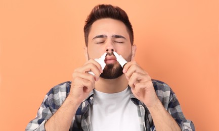 Man using nasal sprays on peach background