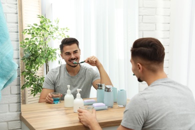 Young man brushing teeth near mirror in bathroom at home