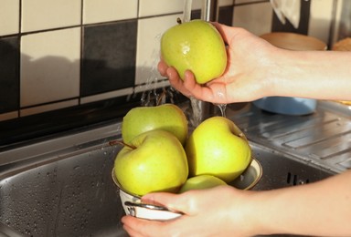 Photo of Woman washing fresh apples in metal colander, closeup