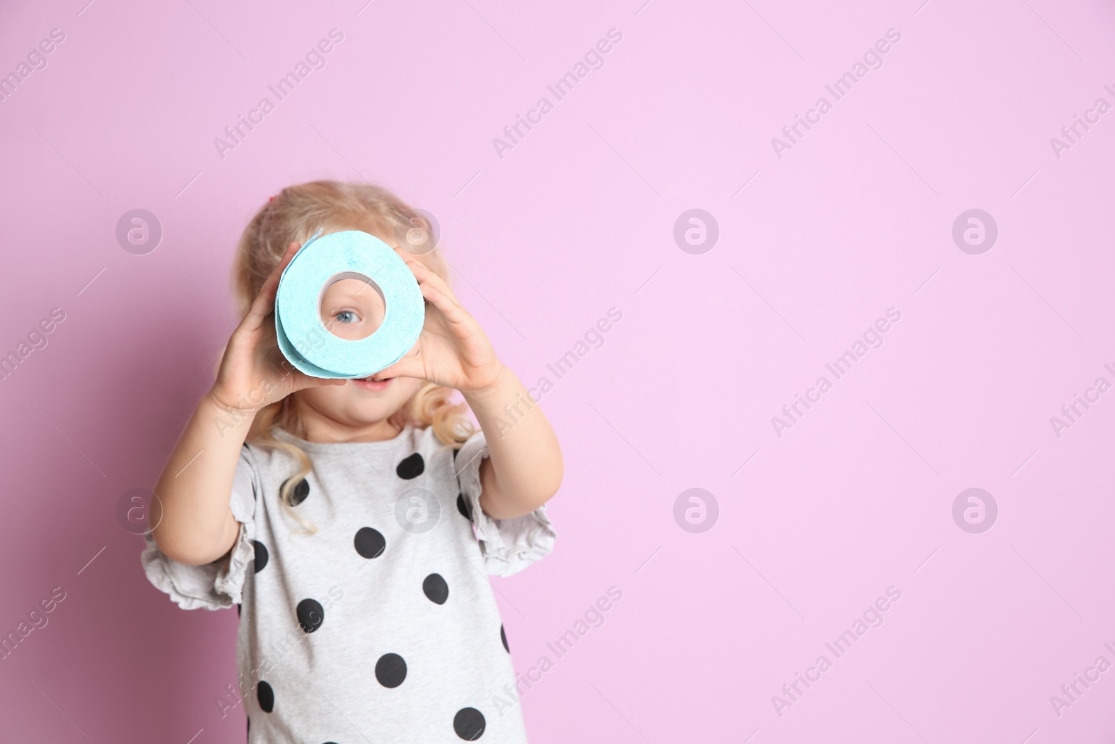 Photo of Cute little girl looking through toilet paper roll on color background. Space for text