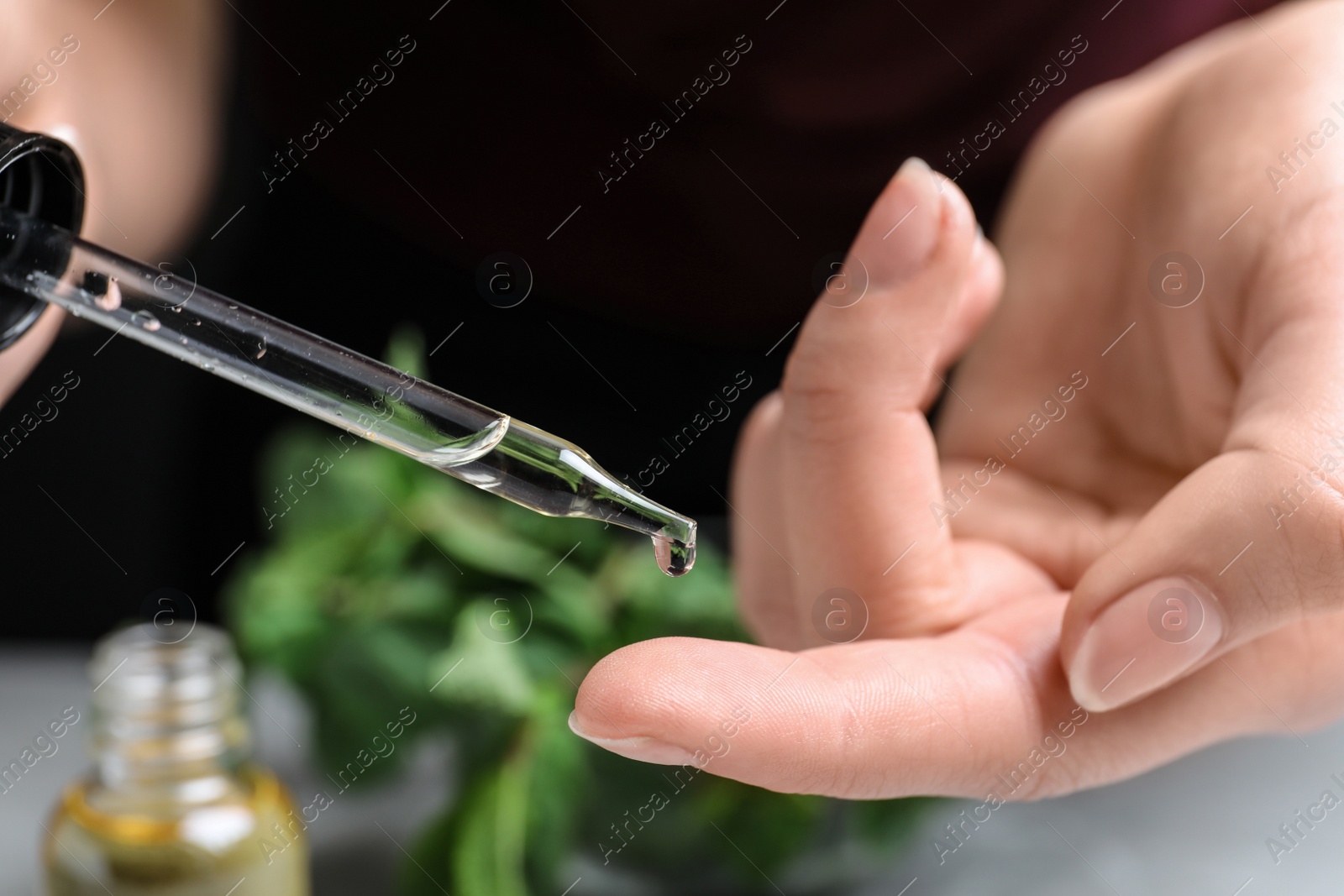 Photo of Woman dripping essential oil onto her finger on blurred background, closeup