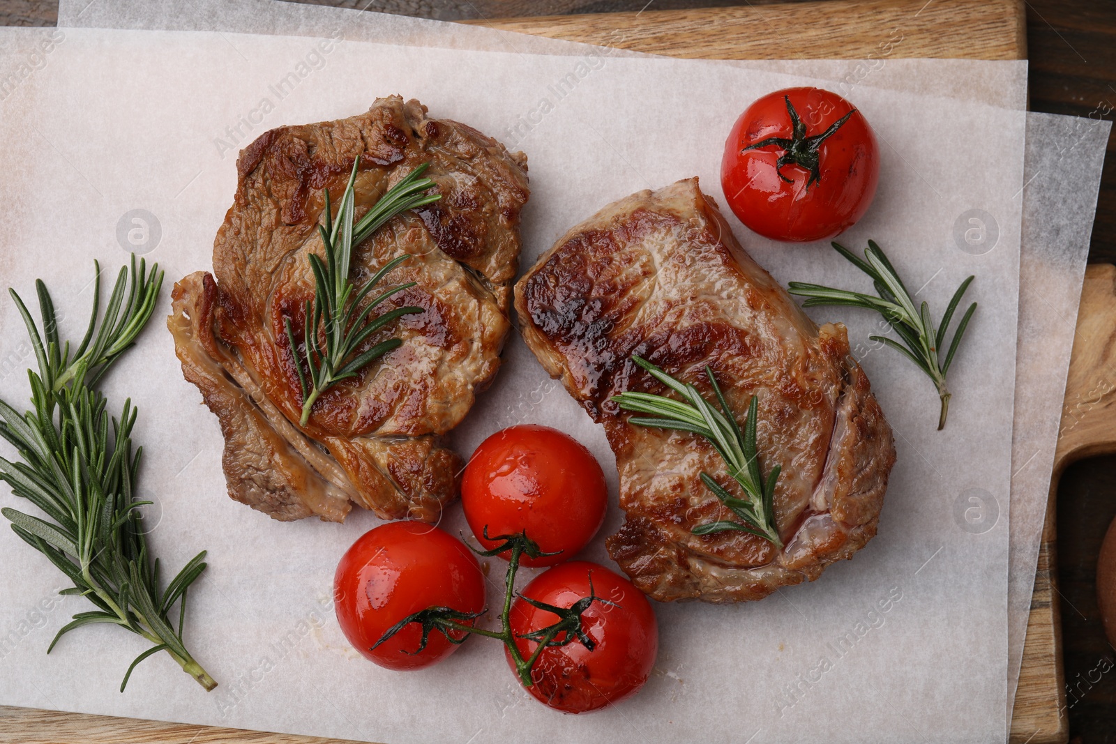 Photo of Delicious fried meat with rosemary and tomatoes on wooden board, flat lay