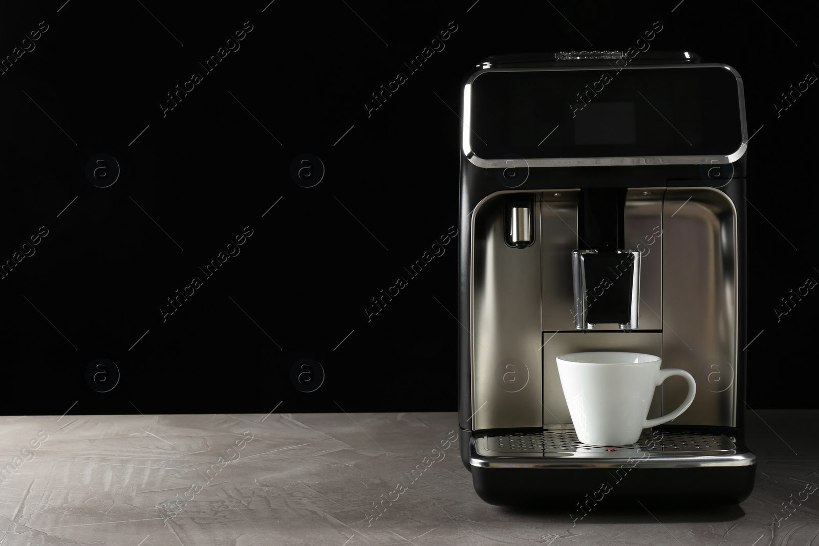 Photo of Modern coffee machine with cup on table against black background. Space for text