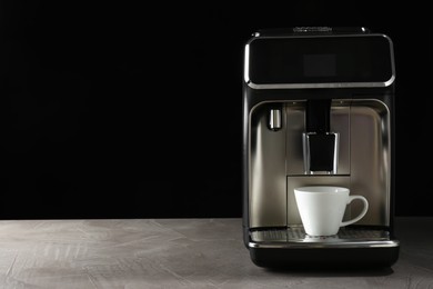 Modern coffee machine with cup on table against black background. Space for text