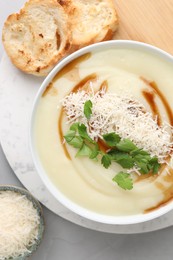 Delicious cream soup with parmesan cheese, soy sauce in bowl and croutons on light grey table, flat lay