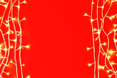 Photo of Christmas lights on red background, top view. Space for text