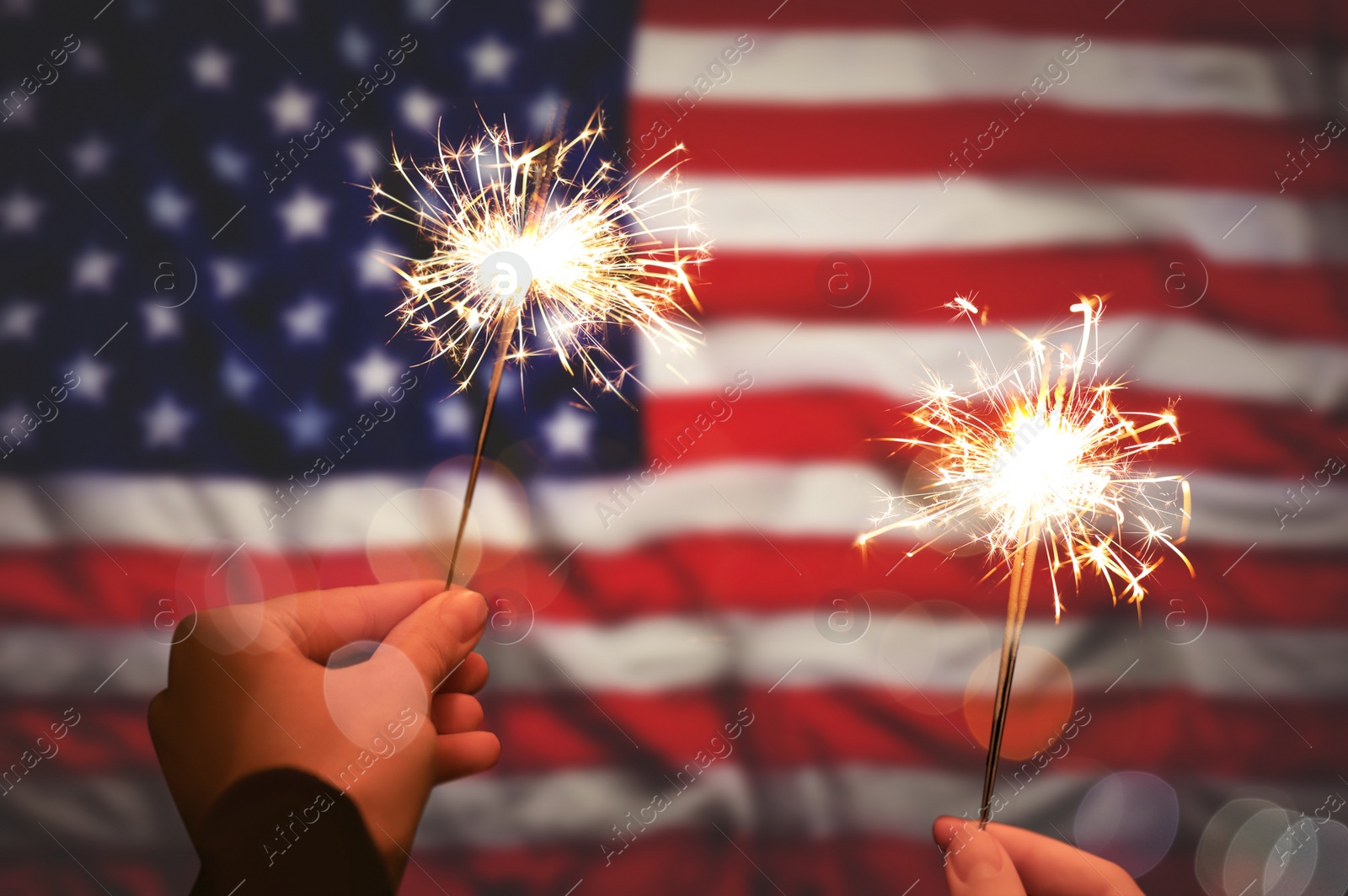 Image of 4th of July - Independence Day of USA. Women holding burning sparklers against American flag, closeup