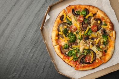 Photo of Delicious vegetarian pizza with mushrooms, cheese and vegetables in box on black table, top view. Space for text