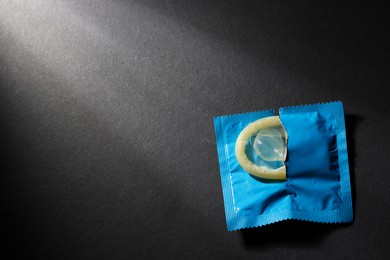 Photo of Condom in torn package on black background, top view with space for text. Safe sex