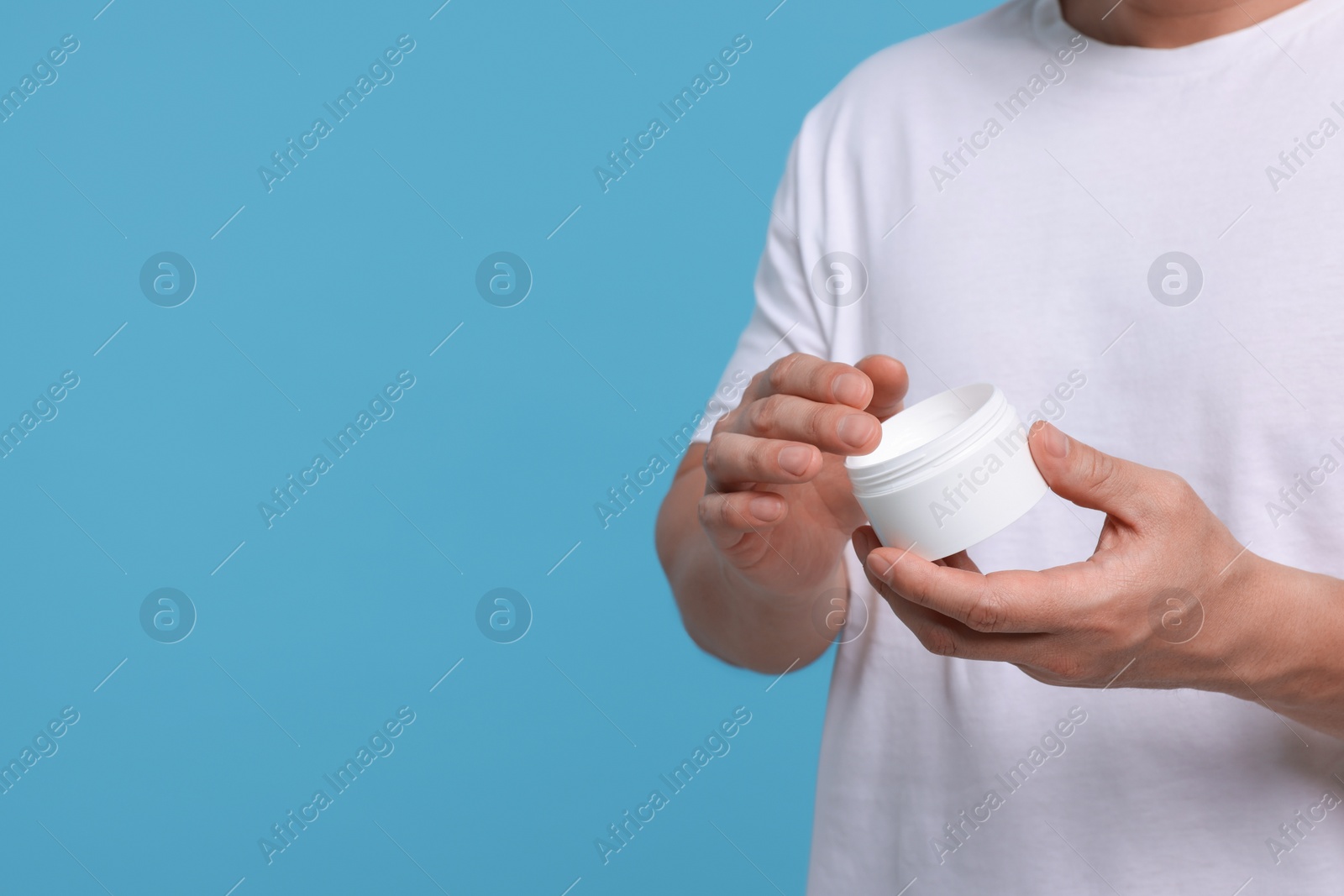 Photo of Man with jar of body cream on light blue background, closeup. Space for text