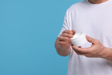 Man with jar of body cream on light blue background, closeup. Space for text