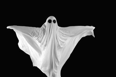 Photo of Creepy ghost. Person covered with white sheet on black background