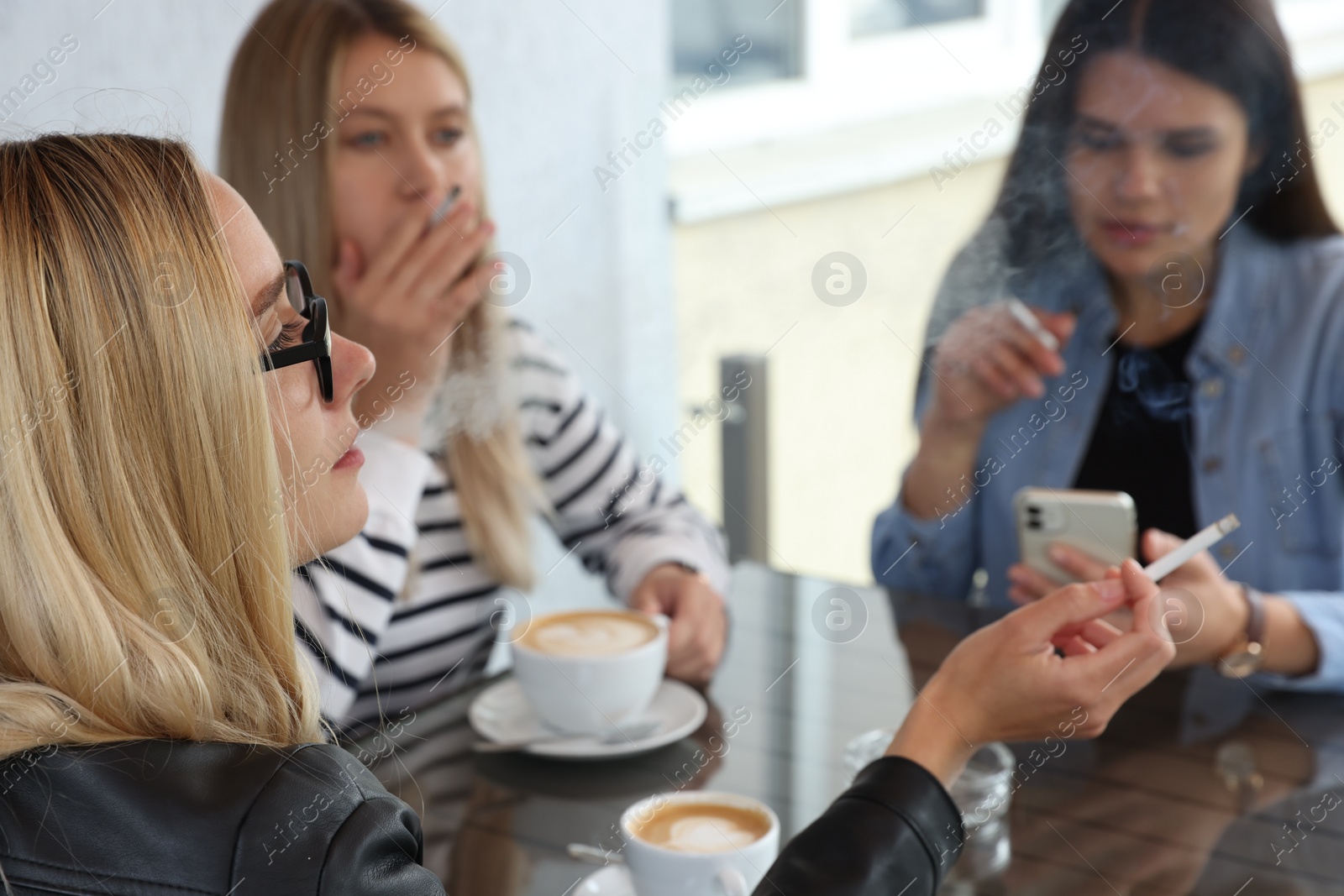 Photo of Women smoking cigarette at table in outdoor cafe