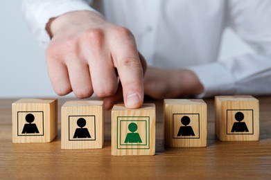 Image of Man putting wooden cube with human green icon ahead of others with black ones at table, closeup