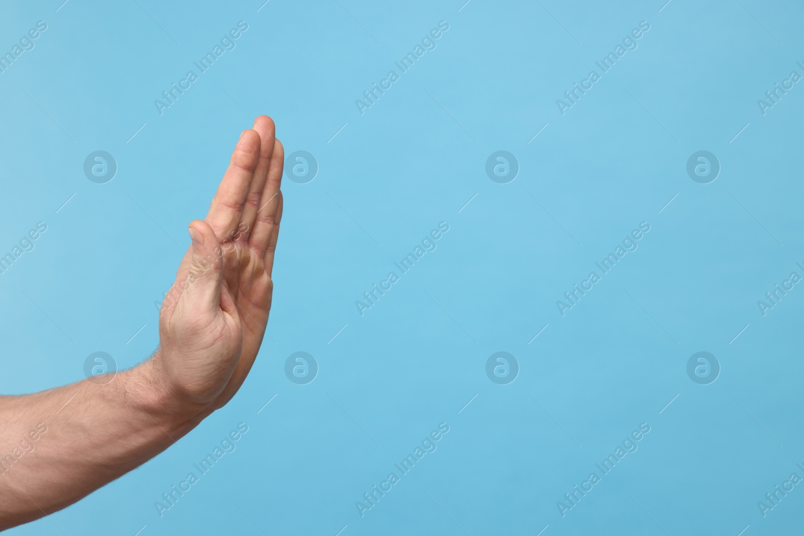 Photo of Man showing stop gesture on light blue background, closeup. Space for text