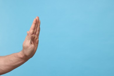 Photo of Man showing stop gesture on light blue background, closeup. Space for text