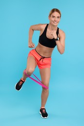 Woman exercising with elastic resistance band on light blue background