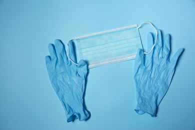 Latex gloves and disposable face mask on light blue background, flat lay. Protective measures during coronavirus quarantine