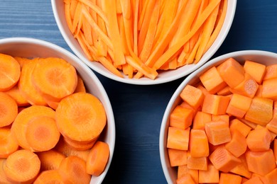 Photo of Bowls with cut fresh juicy carrots on blue wooden table, flat lay