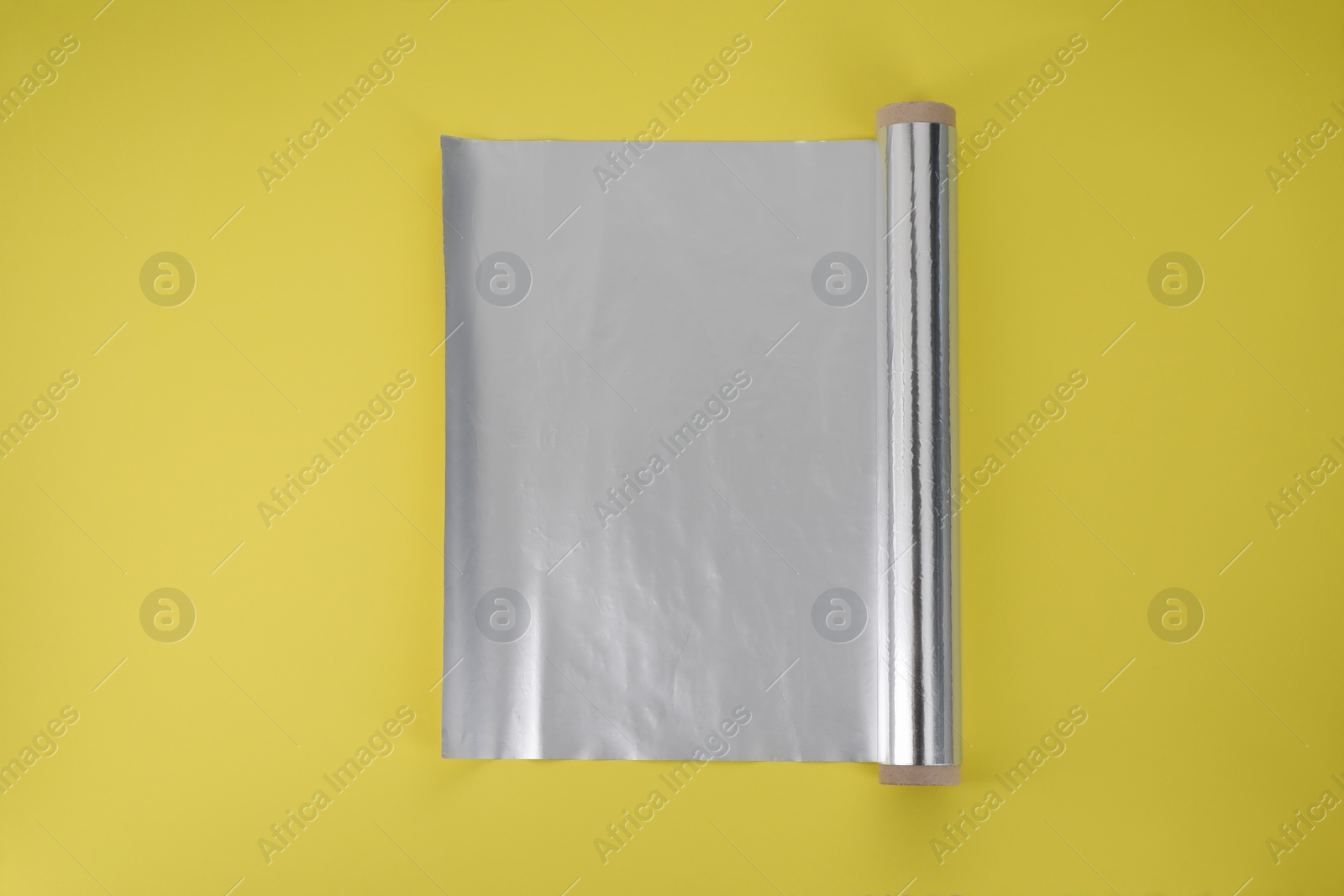 Photo of Roll of aluminum foil on yellow background, top view
