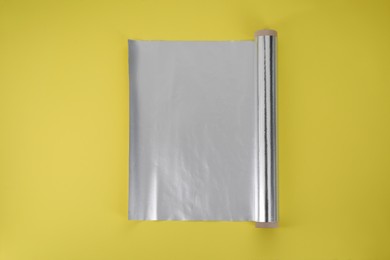 Photo of Roll of aluminum foil on yellow background, top view