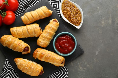 Photo of Delicious sausage rolls and ingredients on grey table, flat lay. Space for text