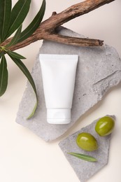 Tube of natural cream, olives, stones and branch with leaves on white background, flat lay