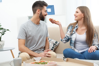 Young couple having pizza for lunch in living room. Food delivery