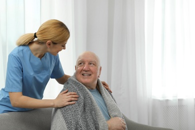 Photo of Nurse covering elderly man with blanket indoors, space for text. Assisting senior people